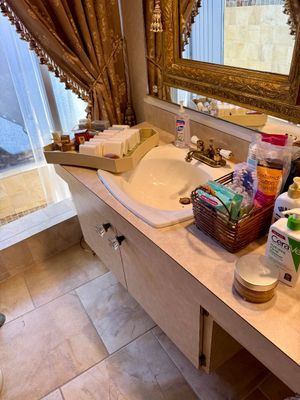 Bathroom vanity counter filled with various toiletries, bar soaps, cotton pads, and lotions under a gold Ornate framed mirror.