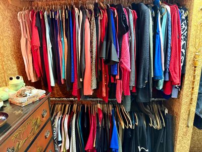 Closet packed with a large collection of women's clothing, including colorful tops, sweaters, and jackets hanging on dual racks.
