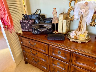 French Provincial style wooden dresser arranged with various women's handbags, decorative angel figurines, and perfume bottles on a...