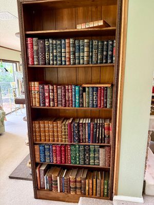 Tall wood bookcase filled with a large collection of vintage leather-bound and decorative hardcover books.