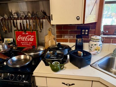 Kitchen counter assortment featuring stainless steel pans, electric skillets, a vintage Coca-Cola sign, a green ceramic teapot, and...