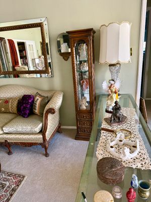 Living room setup featuring a carved wooden curio cabinet filled with angel figurines, alongside a traditional upholstered sofa and...