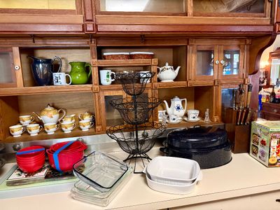 A collection of kitchenware and tableware on a counter in front of an oak hutch, featuring Pyrex glass baking dishes, a black speckled...