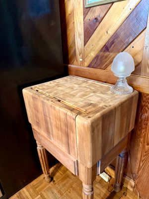 Vintage heavy-duty butcher block kitchen island cart featuring an end-grain wood top, carved turned legs, and a small frosted glass lamp.
