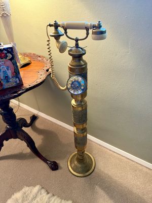 Vintage brass pedestal rotary telephone featuring ornate relief detailing and a cream-colored handset handle.