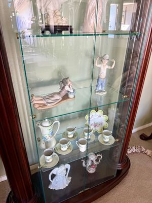 A mahogany curio display cabinet with glass shelves, filled with porcelain figurines including Lladro-style statues and a fine floral tea...