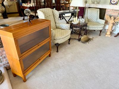 Two-tier wooden barrister bookcase with glass flip-up doors, shown alongside matching patterned upholstered wingback chairs and...