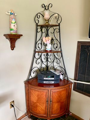 Corner baker's rack style unit featuring wrought iron scrollwork above a wooden cabinet base with parquet door panels, displaying...