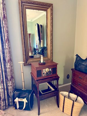 Retro-style tabletop record player and radio sitting on a wooden side table, positioned beneath a large ornate gold-framed wall mirror.