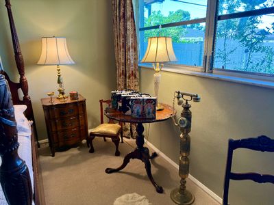 Bedroom corner featuring traditional furniture including a wooden tripod side table, a vintage brass standing candlestick-style...