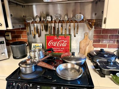 Collection of stainless steel cookware, small kitchen appliances, and antler-handled utensils displayed on a kitchen counter and stove.