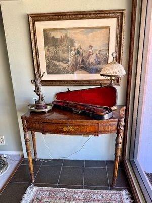 Antique painted wooden console table displaying a bronze figure, a small beaded table lamp, and an open violin case containing a violin,...