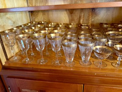 Large collection of vintage crystal stemware and glasses featuring gold filigree rims and etched floral details.