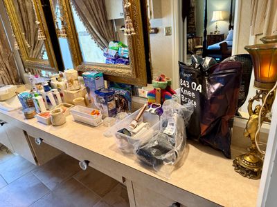 A bathroom vanity top filled with various medical supplies, toiletries, a knee brace in packaging, hair styling tools, and an ornate...
