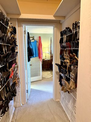 Walk-in closet packed with various women's shoes, heels, and sandals on wall-mounted wire racks, leading into a bedroom.