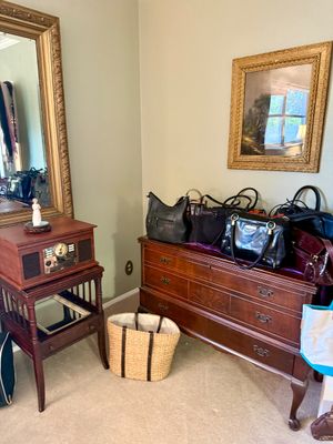 Vintage-style wooden chest of drawers topped with a variety of women's leather handbags, displayed alongside a retro turntable...