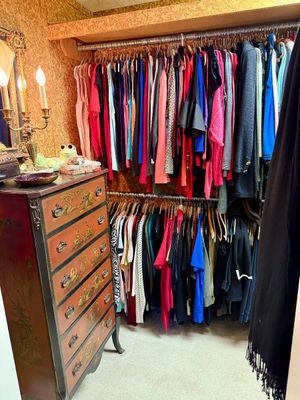 A vintage Asian-style hand-painted Chinoiserie tallboy dresser alongside a closet filled with assorted women's clothing.