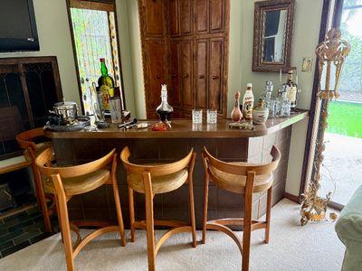 Home bar set with a tiled counter, three mid-century modern curved wooden barstools with upholstered seats, and various barware accessories.