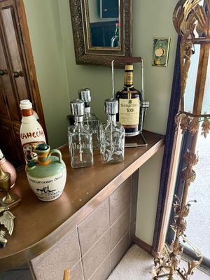 Vintage barware setup including etched glass pump decanters, a large Seagram's V.O. bottle in a metal tilting cradle, a ceramic...