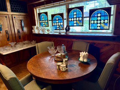 Round wooden dining table with four upholstered armchairs set in a wood-paneled room, featuring a collection of cut glassware, decorative...