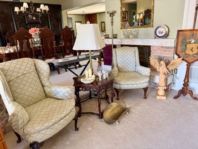 Living room setup featuring a pair of matching patterned wingback armchairs, a carved wooden end table with a brass lamp, a standing...