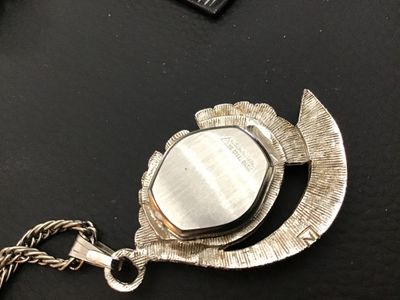 Sale Photo Thumbnail #34: Vintage Belforte pendant watch styled as a necklace. Features an ornate silver-tone, fan-shaped housing set with marcasite-style accents, an oval watch face with silvertone hands and numbers, and a matching chain. The back of the watch casing is marked 'B