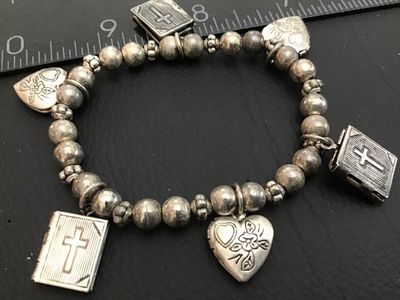 Sale Photo Thumbnail #125: Silver-tone beaded stretch charm bracelet featuring opening Bible book lockets with cross motifs and floral engraved heart lockets. Shows minor wear and tarnish consistent with age.