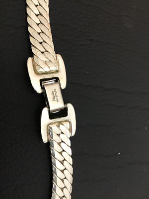 Sale Photo Thumbnail #109: A vintage silver-tone flat herringbone chain necklace by Napier. Features a secure fold-over clasp marked 'Napier PAT. 4,774,743' and 'NAPIER©'. The piece shows a classic flat-link woven design with a shiny finish. In good vintage condition with minor su