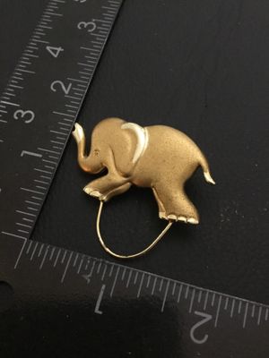 Sale Photo Thumbnail #167: Gold tone elephant brooch / pin clip featuring a textured finish and polished accents with a loop attachment at the bottom. Measures approximately 1.25 inches long by 1.5 inches tall including the loop. Good condition with standard pin bar closure on back