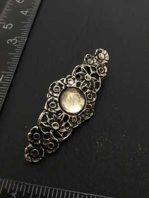 Sale Photo Thumbnail #199: A silver-tone metal brooch featuring detailed openwork filigree, floral motifs, and a central round faux pearl/cabochon accent. Measures approximately 2.25 inches long by 0.75 inches wide. Features a standard pin back with clasp. Good condition with light