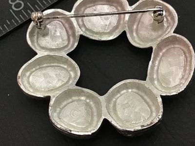 Sale Photo Thumbnail #90: A vintage circular wreath-style brooch featuring textured silver-tone metal set with dark blue/navy enamel or stone cabochons. The back features a crosshatched pattern with a copyright mark and a functional pin back clasp. Measures approximately 1.5 inche