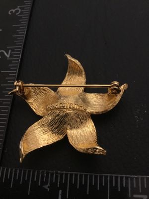 Sale Photo Thumbnail #47: Vintage Sarah Coventry gold-tone textured flower brooch featuring a faux pearl center. Marked 'SARAH COVENTRY' on the back. Measures approximately 2 inches wide. Features a safety clasp on the pin back. In good vintage condition with minimal wear.