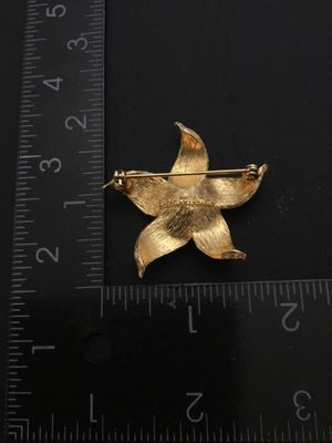 Sale Photo Thumbnail #44: Vintage Sarah Coventry gold-tone textured flower brooch featuring a faux pearl center. Marked 'SARAH COVENTRY' on the back. Measures approximately 2 inches wide. Features a safety clasp on the pin back. In good vintage condition with minimal wear.