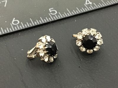 Sale Photo Thumbnail #235: Pair of vintage silver-tone clip-on earrings featuring a central faceted black rhinestone surrounded by a halo of clear rhinestones. Each earring measures approximately 0.5 inches in diameter. Show minor age-appropriate surface wear to metal backing.