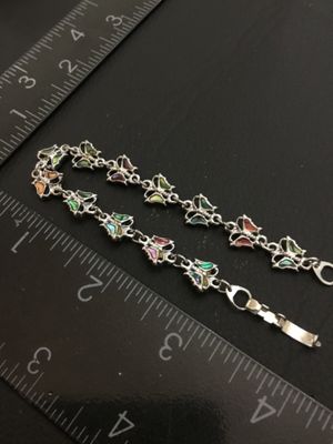 Sale Photo Thumbnail #210: A silver-tone link bracelet featuring connected butterfly links inlaid with colorful crushed shell / abalone inlay. Measures approximately 7 inches long end-to-end with a fold-over clasp. Good condition with minimal signs of wear.