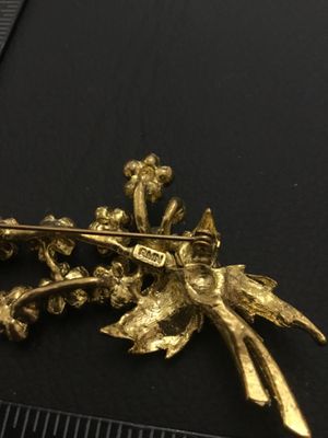 Sale Photo Thumbnail #62: A vintage gold-tone floral bouquet brooch signed RMN, featuring textured leaves and flowers set with sparkling pink rhinestones. Includes a rollover safety clasp on the back. Measures approximately 2.5 inches in length.