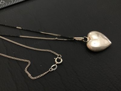Sale Photo Thumbnail #129: A fine silver necklace featuring a puffed heart pendant. The pendant bail is stamped '925' for sterling silver, while the chain clasp tag is stamped '835' alongside a maker's mark/hallmark. Features a curb chain with a spring ring clasp. Shows light tarni