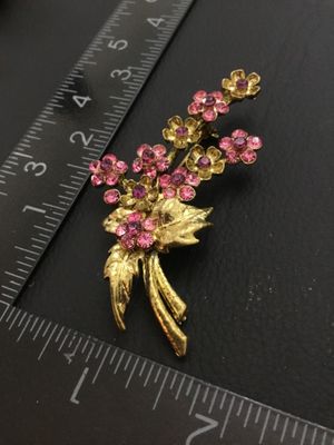 Sale Photo Thumbnail #64: A vintage gold-tone floral bouquet brooch signed RMN, featuring textured leaves and flowers set with sparkling pink rhinestones. Includes a rollover safety clasp on the back. Measures approximately 2.5 inches in length.