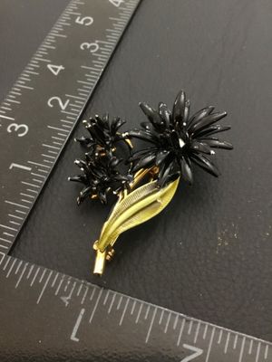 Sale Photo Thumbnail #219: Vintage mid-century style floral spray brooch featuring black enameled flower blossoms and textured gold-tone leaves. Measures approximately 2 inches long by 1.5 inches wide. Overall good vintage condition with pin back clasp in working order; minor ename