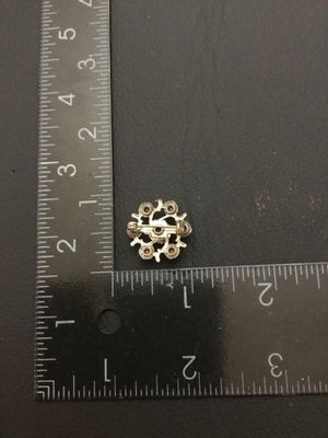 Sale Photo Thumbnail #147: Small vintage silver-tone wreath brooch featuring a center green faceted rhinestone surrounded by six smaller green rhinestones set in stylized branch-like prongs. Features a standard pin back with safety clasp closure. Measures approximately 0.75 inches 