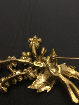 Sale Photo Thumbnail #66: A vintage gold-tone floral bouquet brooch signed RMN, featuring textured leaves and flowers set with sparkling pink rhinestones. Includes a rollover safety clasp on the back. Measures approximately 2.5 inches in length.