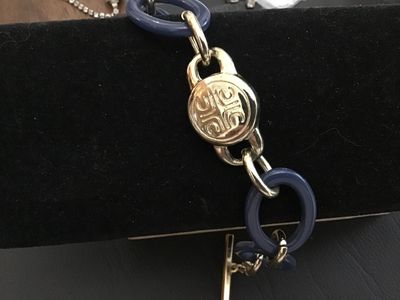 Sale Photo Thumbnail #158: A Liz Claiborne costume jewelry chain bracelet featuring bold blue resin oval links intertwined with gold-tone metal links, a central round engraved medallion, and a branded toggle clasp with an 'LC' charm. In good pre-owned condition with light surface w
