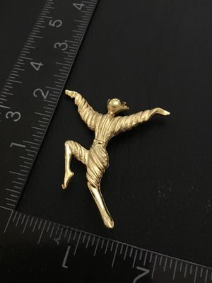 Sale Photo Thumbnail #77: A gold-tone costume jewelry brooch pin depicting a stylized dancing figure with outstretched arms. Features a textured finish and standard rollover pin clasp on the back. Measures approximately 2 inches tall by 2 inches wide. Good vintage condition with l