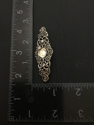 Sale Photo Thumbnail #193: A silver-tone metal brooch featuring detailed openwork filigree, floral motifs, and a central round faux pearl/cabochon accent. Measures approximately 2.25 inches long by 0.75 inches wide. Features a standard pin back with clasp. Good condition with light