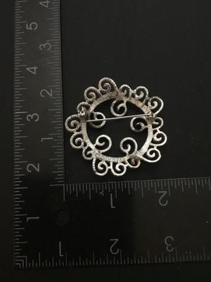 Sale Photo Thumbnail #24: Vintage Sarah Coventry silver-tone brooch featuring an intricate openwork scrollwork design. Marked © SARAH COV on the back. Measures approximately 1.75 inches in diameter. Features a functional rollover safety clasp. Good vintage condition with light we
