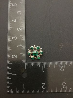 Sale Photo Thumbnail #150: Small vintage silver-tone wreath brooch featuring a center green faceted rhinestone surrounded by six smaller green rhinestones set in stylized branch-like prongs. Features a standard pin back with safety clasp closure. Measures approximately 0.75 inches 