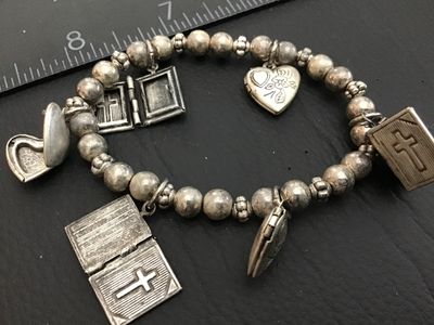 Sale Photo Thumbnail #122: Silver-tone beaded stretch charm bracelet featuring opening Bible book lockets with cross motifs and floral engraved heart lockets. Shows minor wear and tarnish consistent with age.
