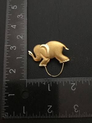 Sale Photo Thumbnail #164: Gold tone elephant brooch / pin clip featuring a textured finish and polished accents with a loop attachment at the bottom. Measures approximately 1.25 inches long by 1.5 inches tall including the loop. Good condition with standard pin bar closure on back