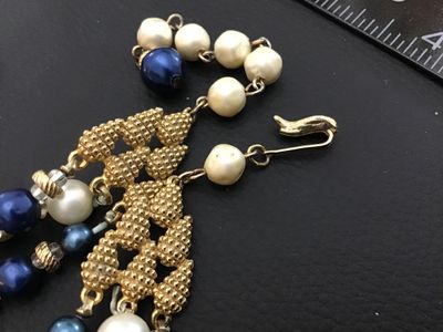 Sale Photo Thumbnail #39: Vintage mid-century style multi-strand statement necklace featuring tiered strands of faux pearls and lustrous blue faux pearls separated by gold-tone spacers. Includes decorative textured gold-tone hardware end connectors and an adjustable hook closure w