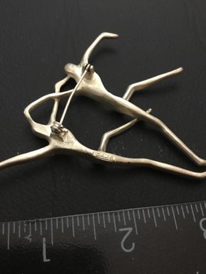 Sale Photo Thumbnail #92: A vintage silver-tone modernist brooch depicting two abstract dancing figures, manufactured by American Jewelry Chain Co. (marked AJC). Features a rollover safety clasp on the back. Measures approximately 2.5 inches wide by 2.25 inches high as shown again